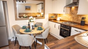 A modern kitchen with a round dining table, grey chairs, and a large mirror above the table. - Rose Cottage - 2 Bedroom Cottage - Penally (Tenby)