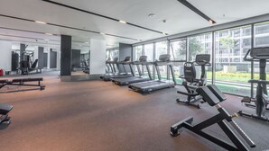 A modern gym with treadmills, weight machines, and a large window offering a view of the city. - Stayshort - 1 Bed in Business Bay Sleeps 2 With City Views (Dubai)