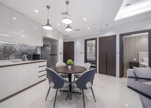 A modern kitchen with a dining area, featuring a central island, pendant lighting, and a view into the adjacent bedroom. - Stayshort - 1 Bed in Business Bay Sleeps 2 With City Views (Dubai)