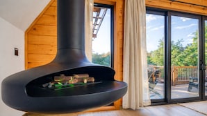 Un interior moderno con una estufa de leña, paredes de madera y una puerta de vidrio que da a una terraza exterior.