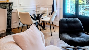 Ein Zimmer mit Esstisch, Stühlen, einer Couch, einem schwarzen Sessel, einem Bild an der Wand und einem Fenster mit Blick ins Grüne.