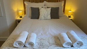 Een opgemaakt bed met witte lakens, twee kussens en twee opgerolde handdoeken op het bed.