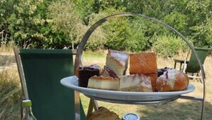 Een drielaags taartplateau met diverse gebakjes en belegde broodjes, een fles water en een glas water op een buitentafel.