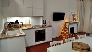 Une cuisine moderne avec des meubles blancs, un four encastré et un coin repas comprenant une table et des chaises blanches.