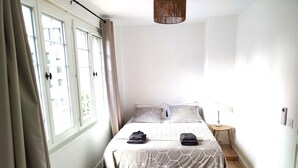 Une chambre à coucher avec un lit, deux oreillers, une table de chevet avec une lampe et une fenêtre avec des rideaux.
