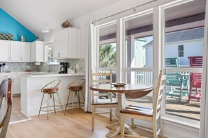A bright kitchen with white cabinets, a blue accent wall, and a large window overlooking a deck with colorful chairs.