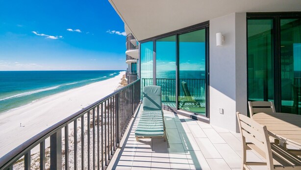 A balcony with a view of the beach, a lounge chair, and a table. - Phoenix Ix 1107 2 Bedroom Condo (Orange Beach)