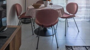 Ruokailutila, jossa on pyöreä pöytä, neljä tuolia, maljakko kukkineen ja riippuvalaisin.