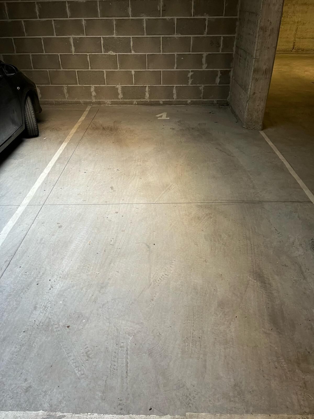 Eine Parkgarage mit Betonboden, Ziegelwand und einer Betonstütze.