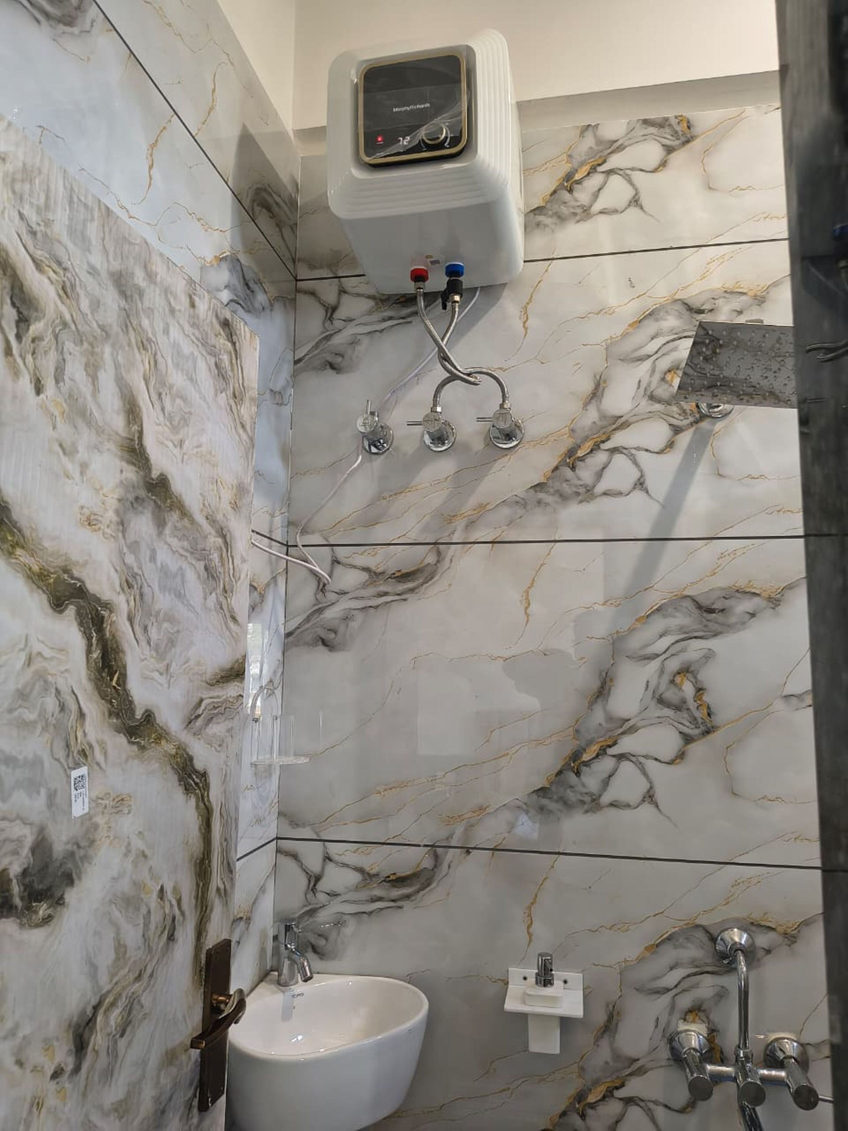 Une salle de bain aux murs recouverts de marbre, avec un lavabo blanc et une douchette à main.
