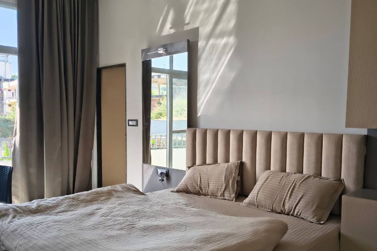 A modern bedroom with a large bed, a headboard, and a view of the outdoors through a window.