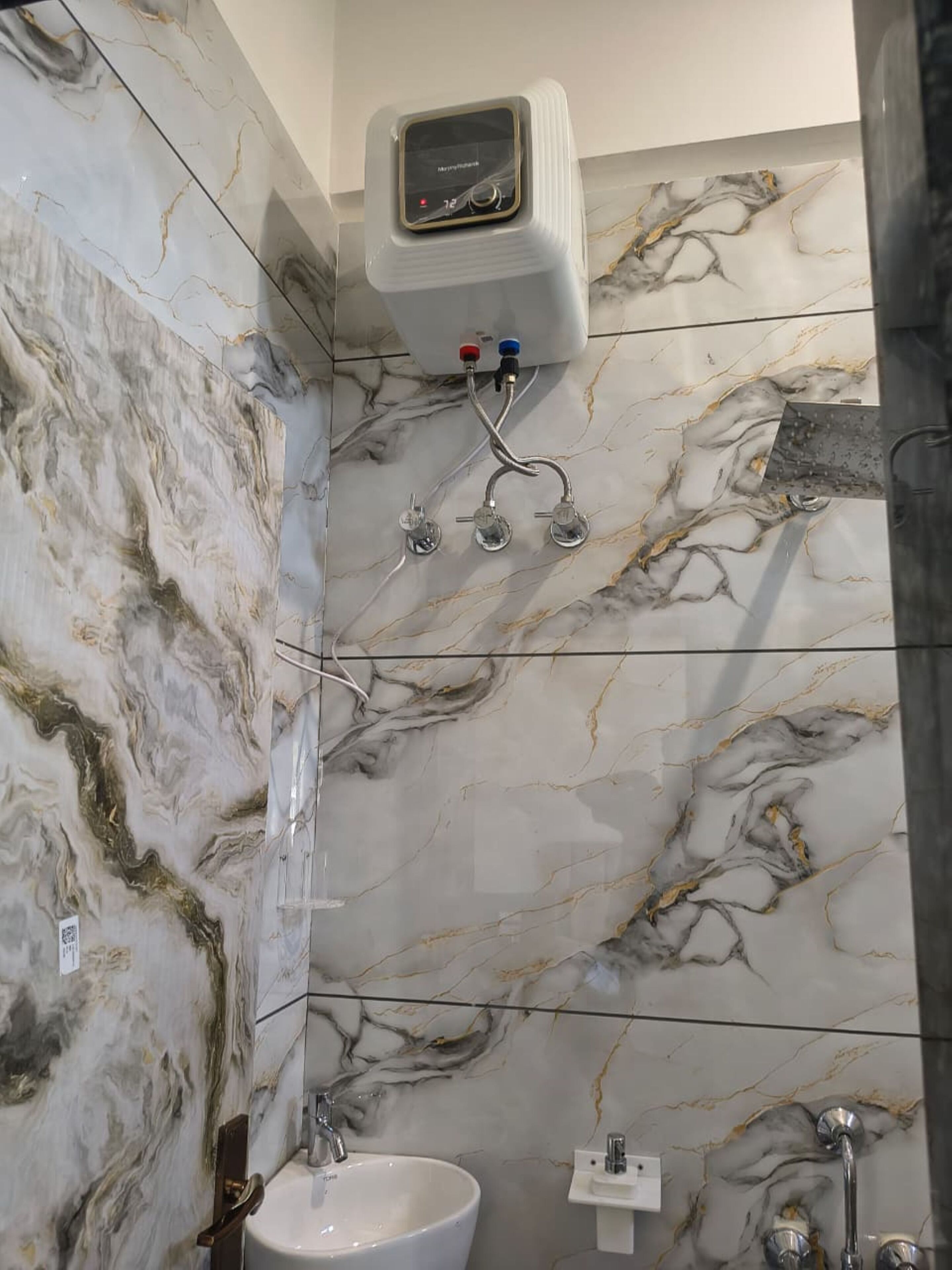Ένα μπάνιο με μαρμάρινοι τοίχους, έναν λευκό νιπτήρα και μια αποσπώμενη κεφαλή ντους.