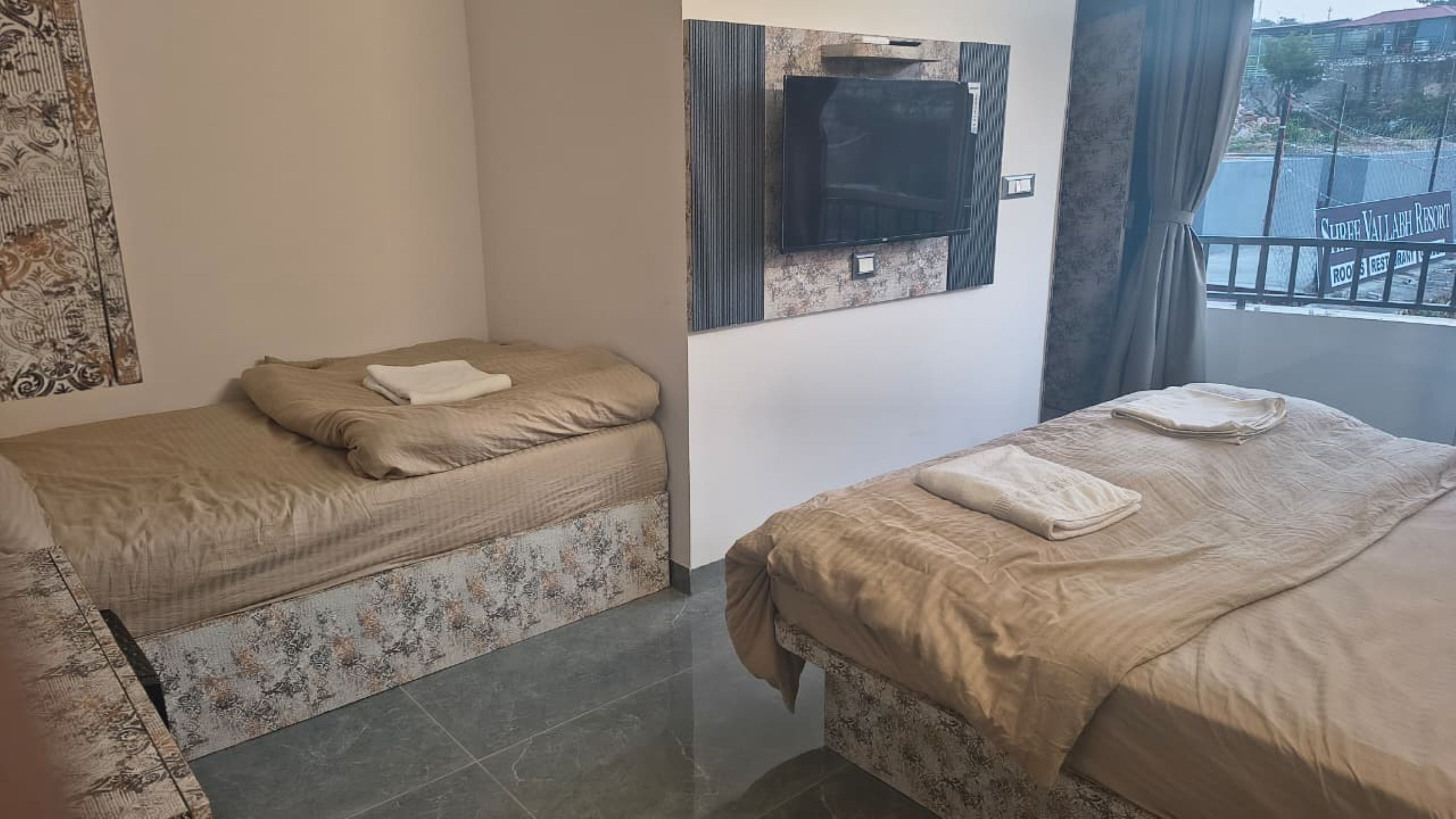 A hotel room with two beds, a flat-screen TV mounted on the wall, and a view of the outside.