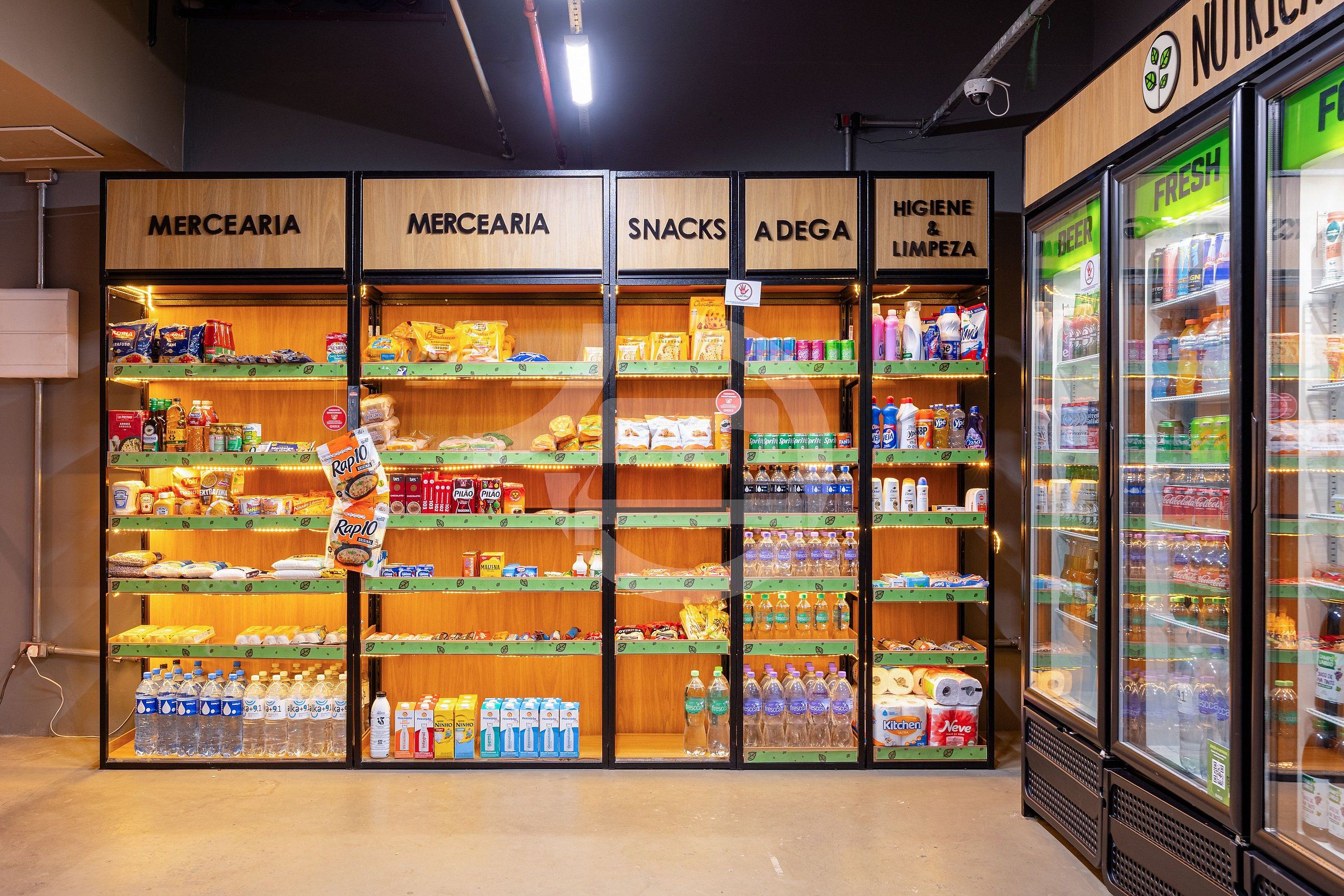 A grocery store interior with sections labeled MERCEARIA, SNACKS, ADEGA, and HIGIENE & LIMPEZA, featuring shelves stocked with various products.