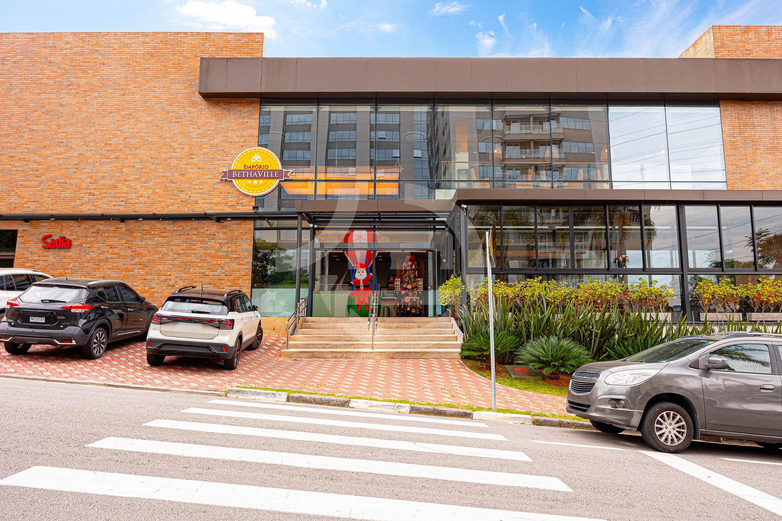 Um edifício moderno com entrada de vidro, uma placa com 'Emporio Bethavia' e carros estacionados na frente.
