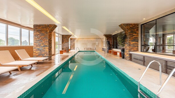 Una piscina interior con sillones de descanso, detalles de piedra y grandes ventanales.