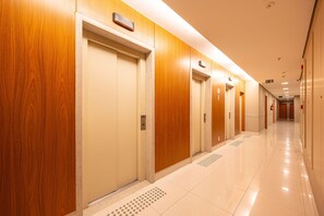 A hotel corridor with wooden doors, a tiled floor, and a sign indicating the direction to the elevator.
