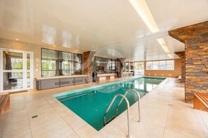 An indoor swimming pool with a clear view of the pool area, a seating area with a bench, and a stone accent wall. - Premium Modern Studio in Alphaville (Santana de Parnaíba)