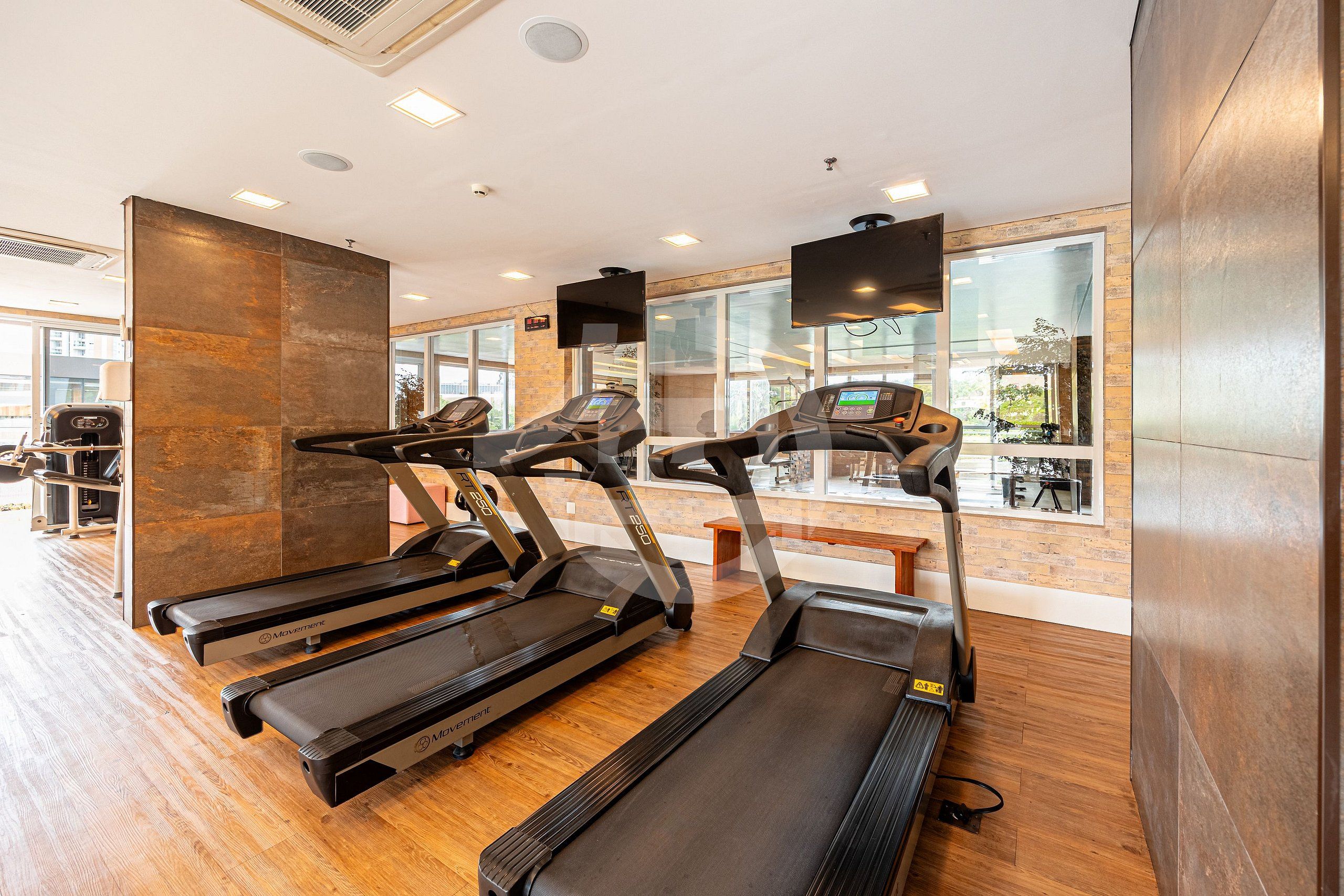 A gym with treadmills, a wooden floor, a large mirror, and a view of the outside.