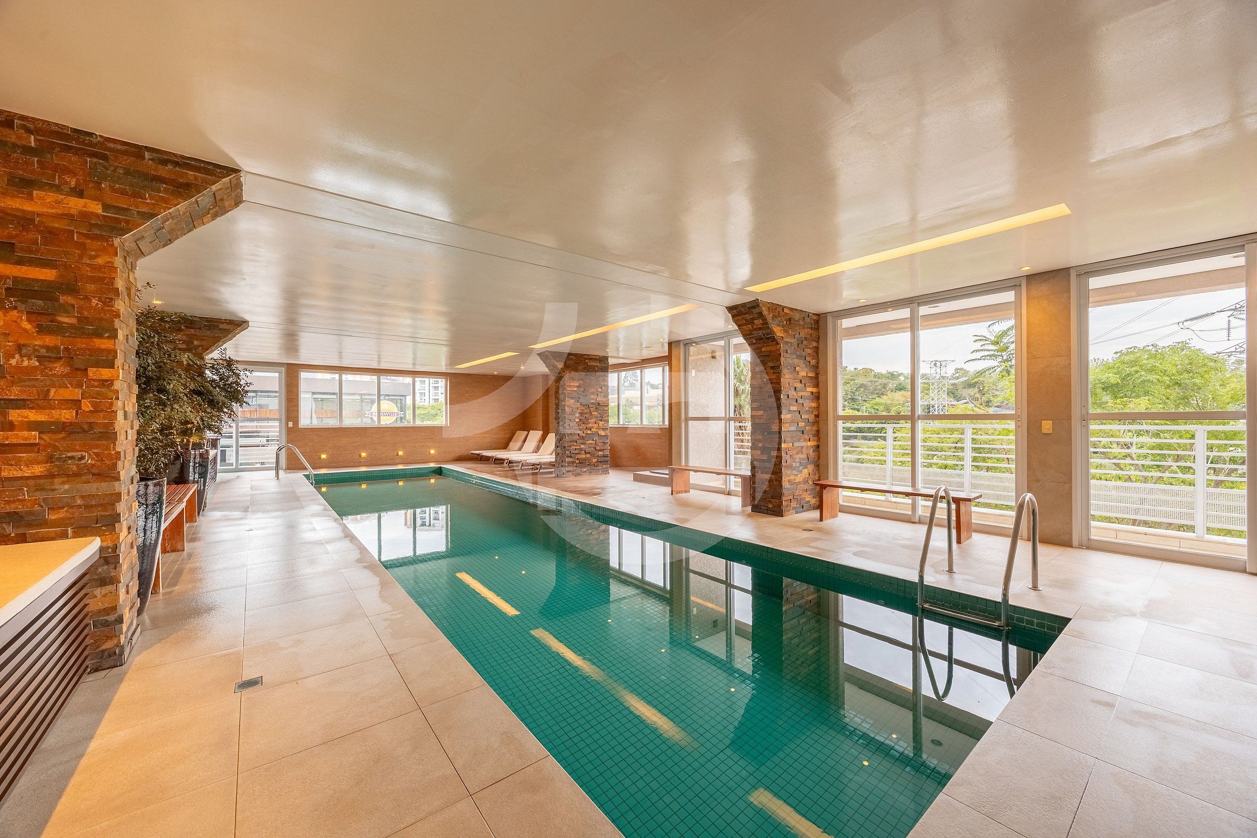 Una piscina interior con vistas despejadas, sillas de descanso y una pared de ladrillo.