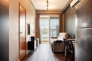 A compact hotel room with a bed, a desk with a chair, a television, and a large window.