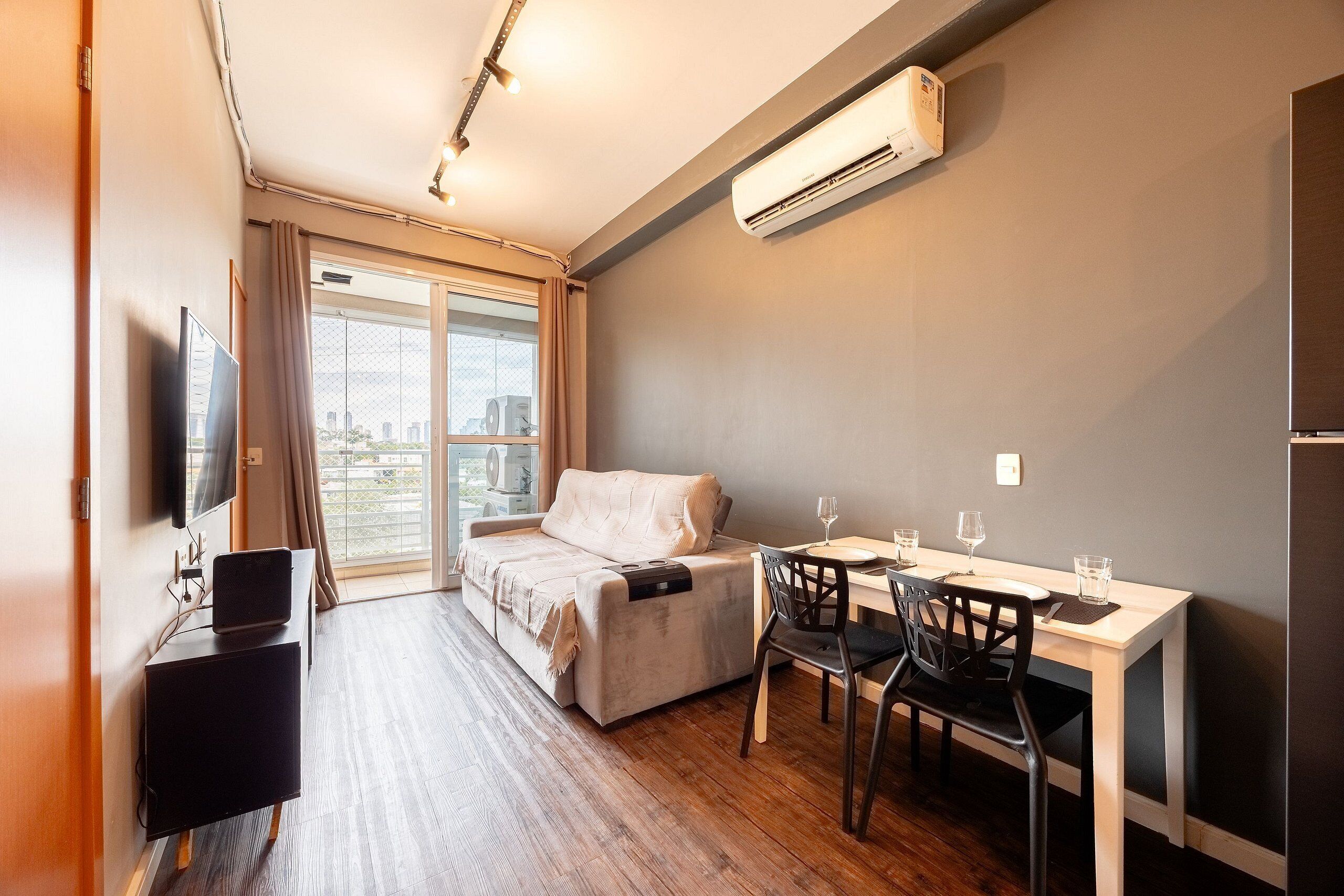 Una habitación moderna con sofá, una mesa de comedor con sillas, televisor y aire acondicionado.