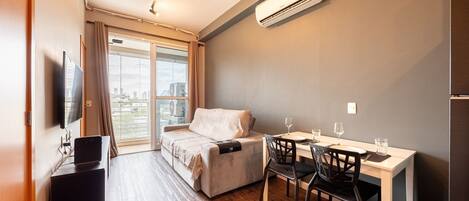 Una habitación moderna con sofá, una mesa de comedor con sillas, televisor y aire acondicionado.