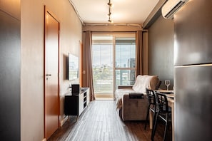 A compact hotel room with a bed, a desk with a chair, a television, and a large window. - Premium Modern Studio in Alphaville (Santana de Parnaíba)