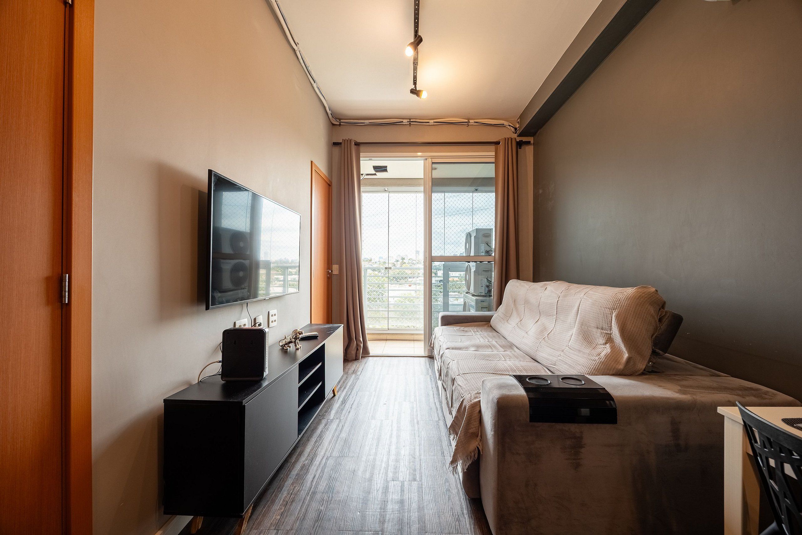 A compact hotel room with a bed, a TV, a desk, and a view of the outdoors.