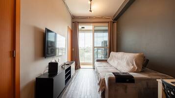 A compact hotel room with a bed, a TV, a desk, and a view of the outdoors.