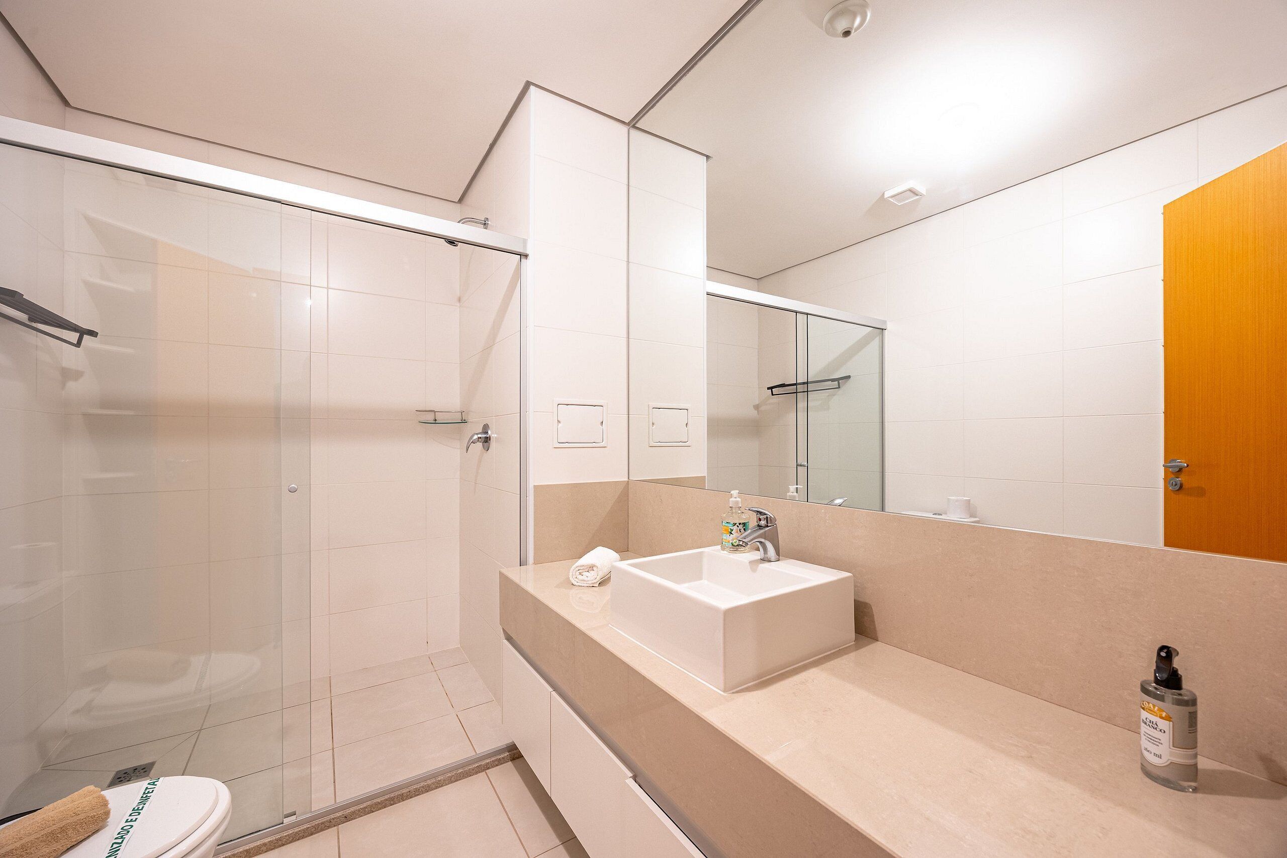 A modern bathroom with a glass shower enclosure, a white sink, and a wooden door.