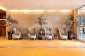 A reception area with four armchairs, two large potted plants, a fire extinguisher, and a glass wall. - Premium Modern Studio in Alphaville (Santana de Parnaíba)