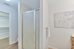 A bathroom with a glass shower door, a towel rack, and a starfish artwork on the wall.