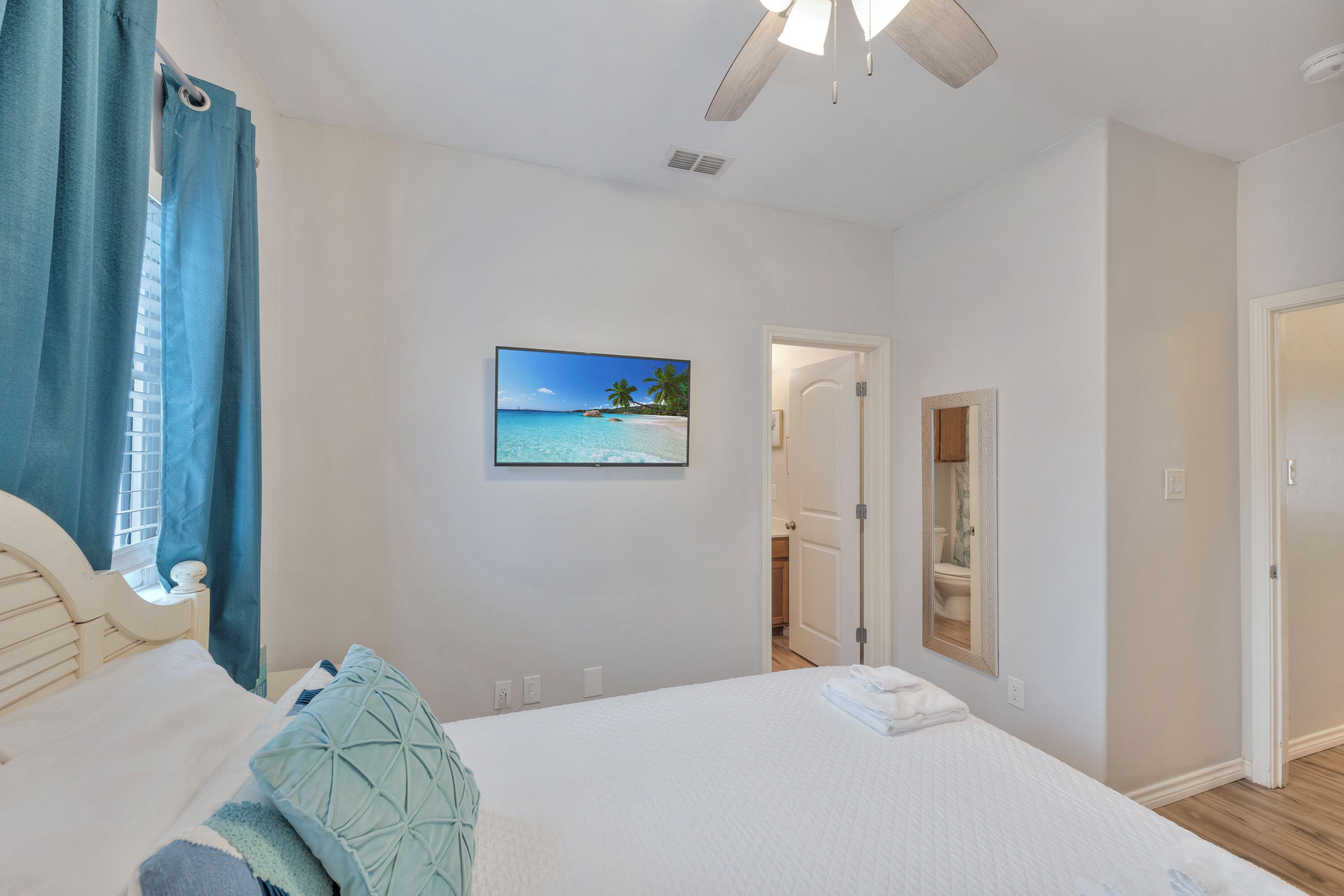 Una camera da letto con un letto, una ventola a soffitto, una TV a parete e una porta che dà su un bagno.