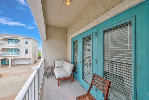 A balcony with a sofa and a wooden chair, a turquoise door, and a view of a building with a balcony.