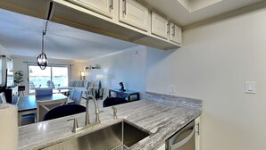 A modern kitchen with a marble countertop, stainless steel sink, and white cabinetry. - Regency Towers #401 East | Gulf Front, Pool, Pickleball/Tennis (Pensacola Beach)