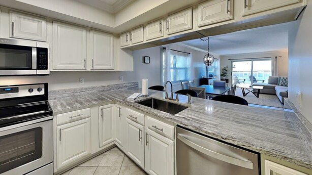 A modern kitchen with white cabinetry, a granite countertop, stainless steel appliances, and a dining area with a view. - Regency Towers #401 East | Gulf Front, Pool, Pickleball/Tennis (Pensacola Beach)