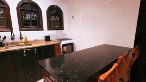 A kitchen with a black granite countertop, wooden chairs, and a brick column. - Chácara Recanto da Coruja - São Pedro, SP (São Pedro)