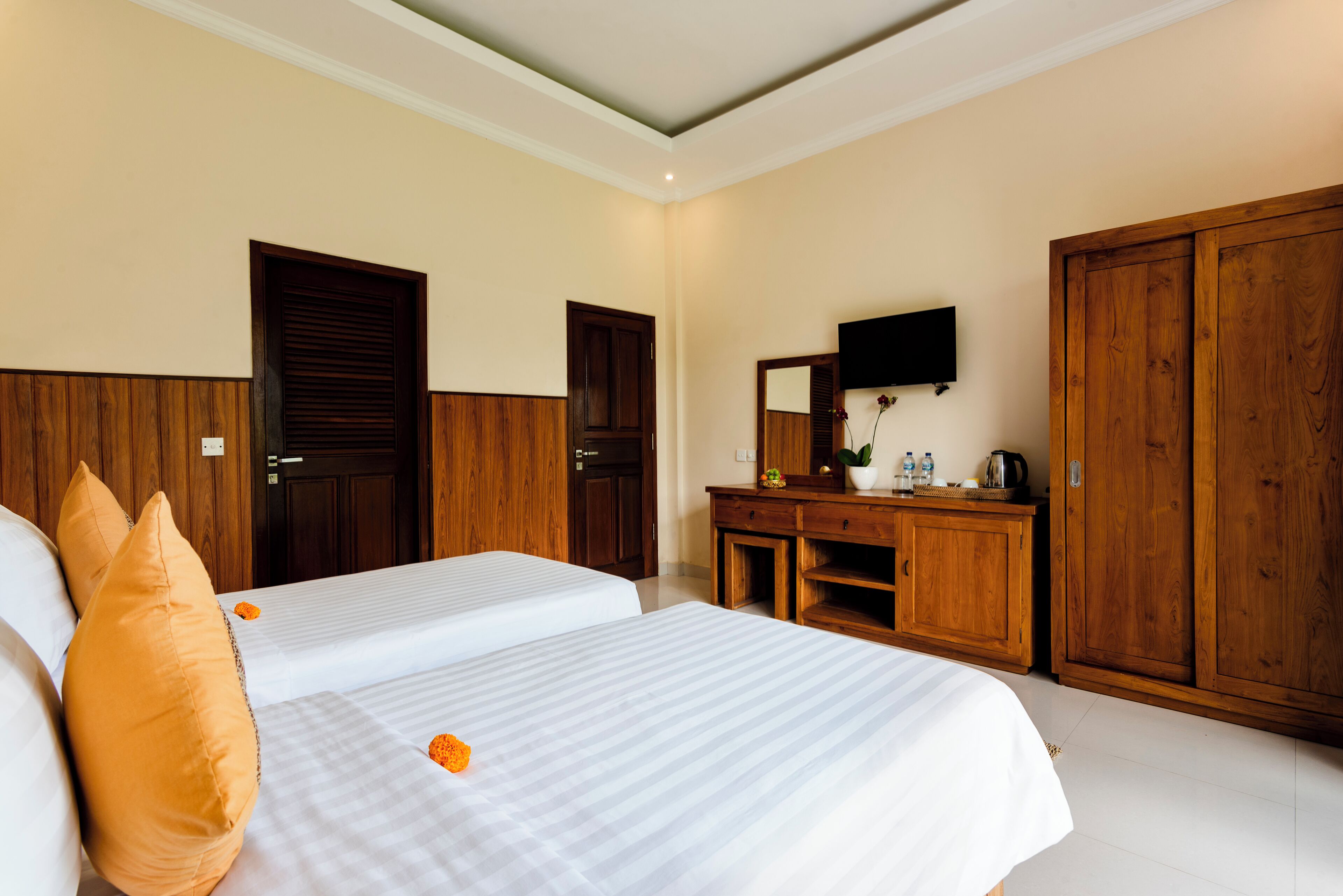 A hotel room with two beds, wooden wardrobe, a desk with a mirror, and a television.