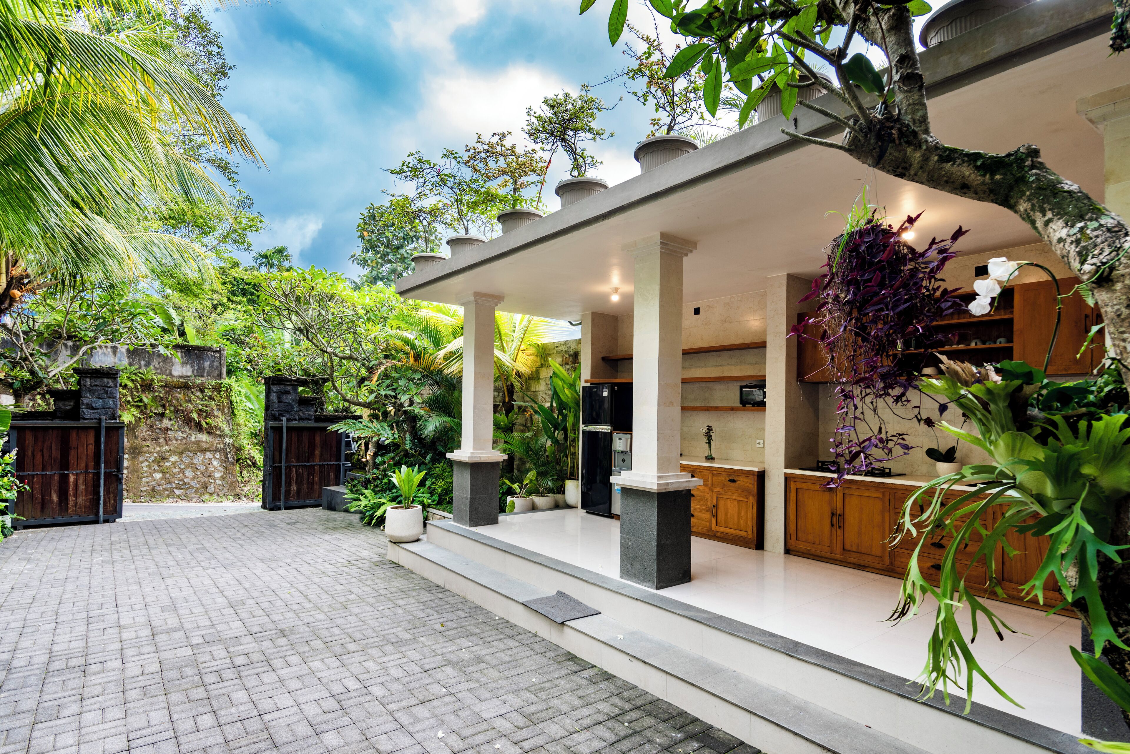 A covered outdoor area with a paved walkway, stone pillars, and a wooden counter with cabinets.