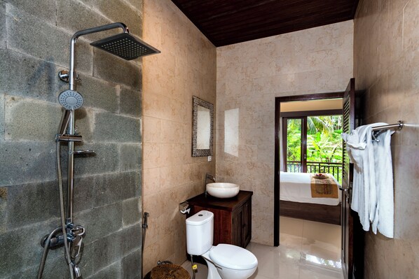A bathroom with a stone shower, a sink, and a toilet. There is a window with a view of greenery outside. - Oka Suite Ubud by Dhananjaya Hospitality (Sebatu)