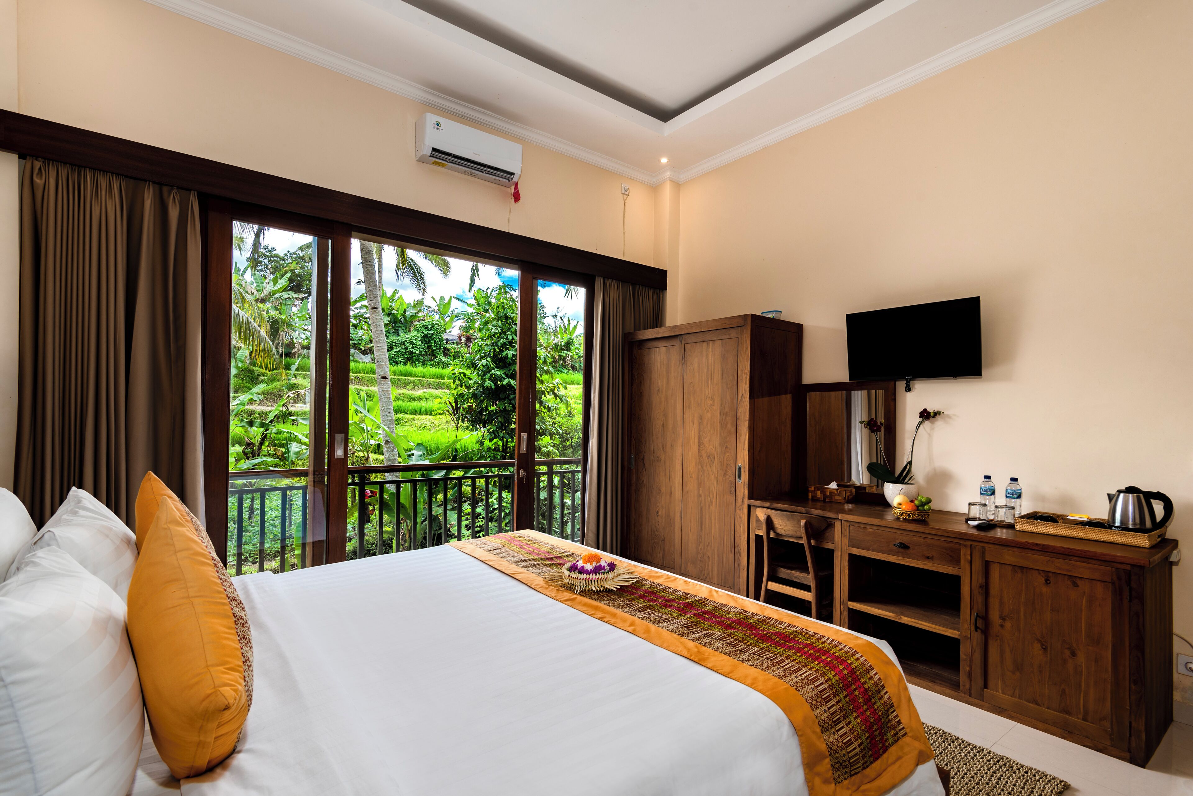 Habitación de hotel con cama, escritorio, televisor y vista a un jardín exuberante.