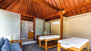 Una habitación con techo de madera, una camilla de masaje, un sillón de masaje, un sofá y una mesita con un jarrón de flores.
