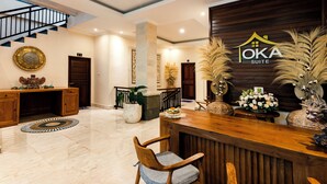 Un área de recepción con un escritorio de madera, sillas, una escalera y una pared decorativa con un logo.