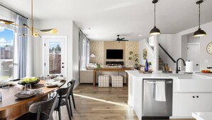 Eine moderne Küche mit einer zentralen Kochinsel, einem Essbereich mit Holztisch und einem großen Fenster mit Blick ins Freie.