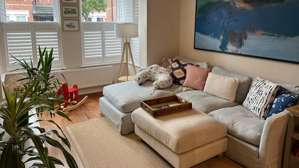 Una sala de estar acogedora con un sofá, un reposapiés y un cuadro grande en la pared.
