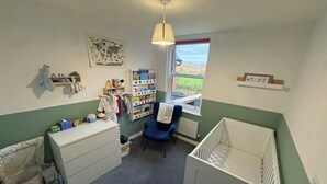 Una habitación infantil con una cuna, un cambiador, una silla y una estantería.