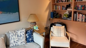 Una sala de estar acogedora con un sofá, una silla, una estantería y un cuadro en la pared.