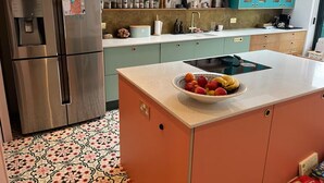 Una cocina con un refrigerador de acero inoxidable, un tazón de fruta sobre la encimera, gabinetes color turquesa y piso estampado.