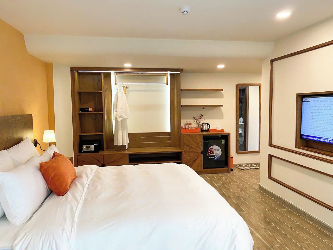 A hotel room with a large bed, a wardrobe, a desk with a computer, and a television.